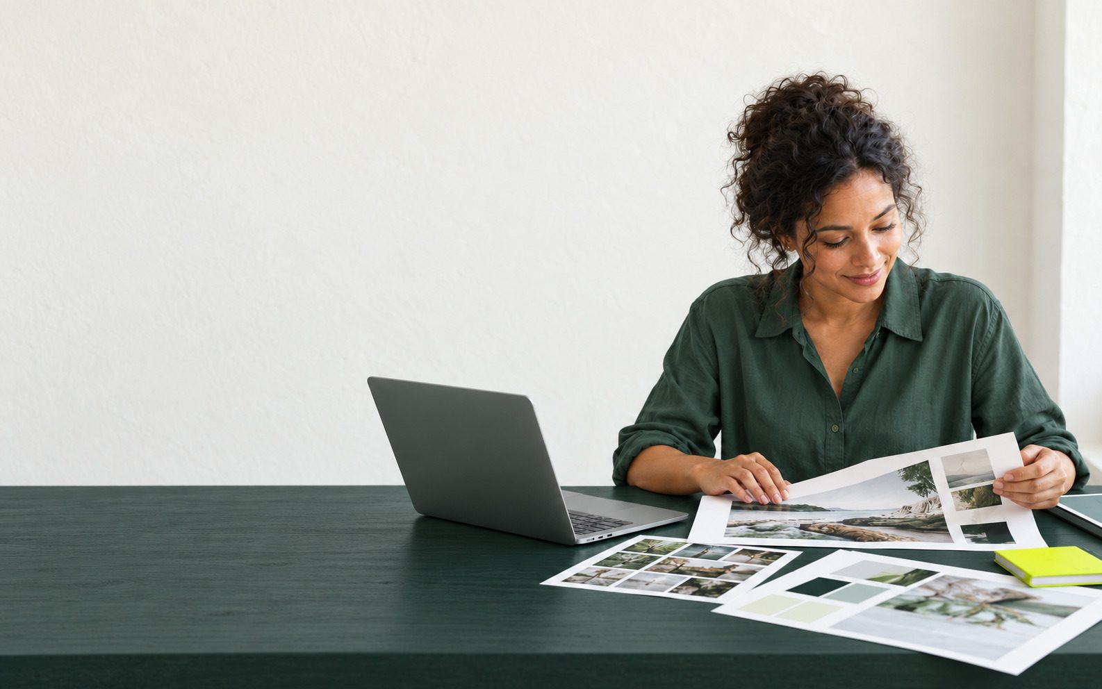 A marketer smiles over printed photo sheets at her desk, the brand’s pictures laid out in front of her